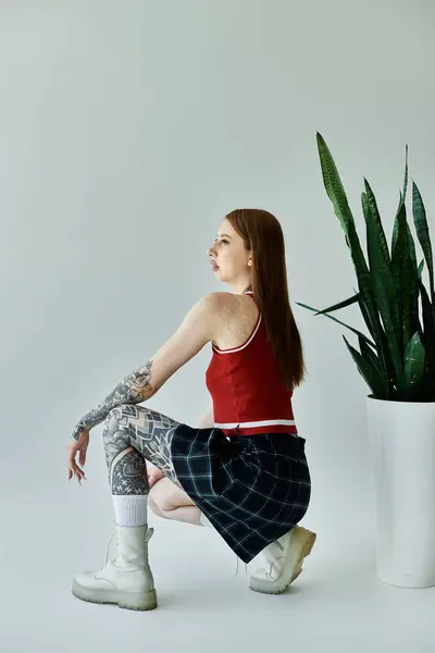 A young woman with tattoos on her arms and legs poses in a red tank top and plaid skirt. She is sitting in a relaxed pose — Stock Photo