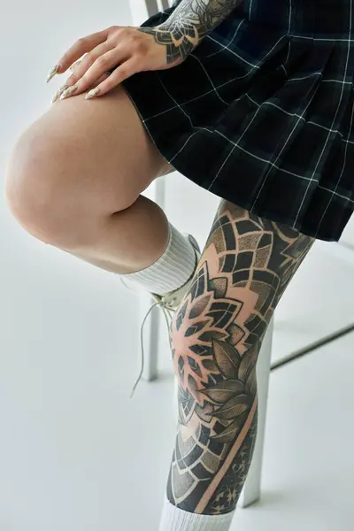 A close-up shot of a young womans tattooed leg in a plaid skirt. — Stock Photo