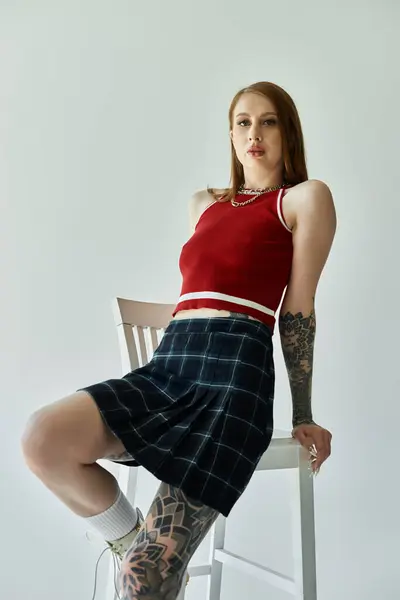 Una giovane donna in canotta rossa e gonna a quadri posa per un servizio di moda, in mostra i suoi tatuaggi e lo stile giovanile. — Foto stock