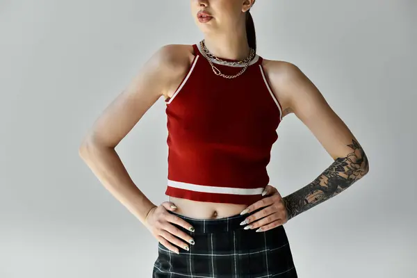 A young woman with tattoos poses in a red tank top and plaid skirt, exuding confidence and style. — Stock Photo