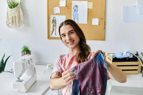 A young man smiles as he shows off a restored shirt in his DIY clothing restoration atelier. — Stock Photo
