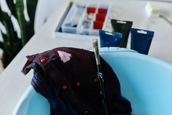 Un pennello poggia accanto a una camicia scartata in un lavandino, suggerendo il processo di rinascita creativa che avviene all'interno dell'atelier.. — Foto stock