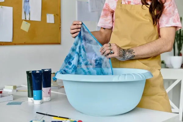 A young man dyes a fabric in a basin, part of his sustainable clothing restoration atelier. — Stock Photo
