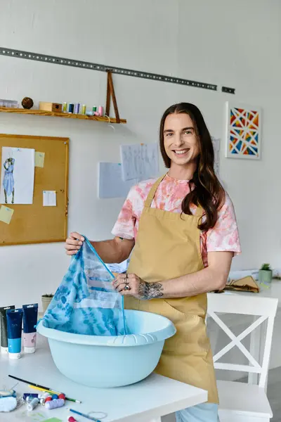 Un joven sonríe mientras sostiene una prenda durante un proyecto de restauración de ropa en su taller sostenible. - foto de stock