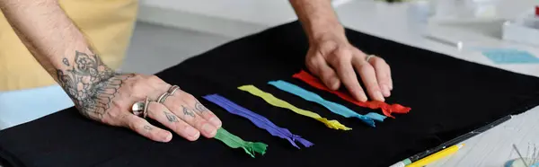 Una mano tatuada selecciona cuidadosamente cremalleras de colores para un proyecto de restauración de ropa, mostrando el meticuloso trabajo de un taller de moda sostenible. - foto de stock