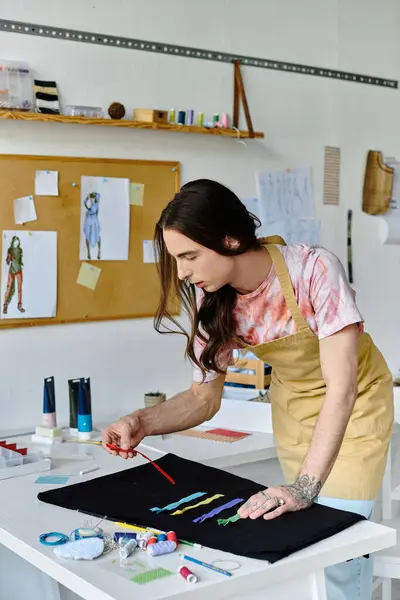 Un joven aplica cuidadosamente tinte a una prenda desechada en su taller de restauración de ropa. Inhala nueva vida en los artículos antiguos, promoviendo prácticas de moda sostenibles. - foto de stock