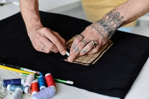 Ein Mann mit einer stark tätowierten Hand markiert ein Stück Stoff mit einem Kreidestift, während er an seinem Kleiderrestaurierungsprojekt arbeitet. — Stockfoto