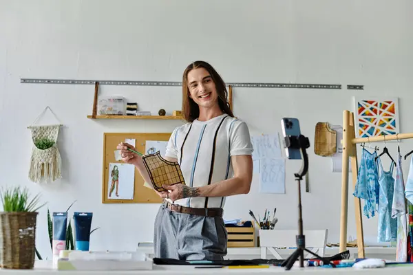 Un joven, dueño de un taller de restauración de ropa de bricolaje, sonríe mientras demuestra una técnica de restauración de prendas. - foto de stock