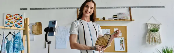 A young man smiles as he holds a piece of clothing in his studio, showcasing his passion for sustainable fashion and clothing restoration. — Stock Photo