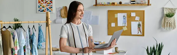 A young gay man, owner of a DIY clothing restoration atelier, works on his laptop while surrounded by clothing items ready to be given new life. — Stock Photo