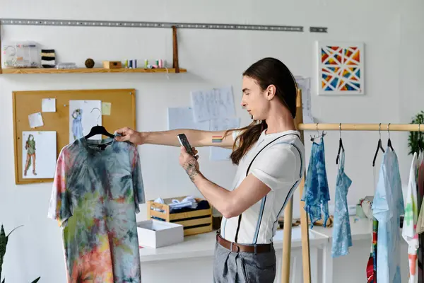 A young man photographs a tie-dye shirt in his DIY clothing restoration atelier. — Stock Photo