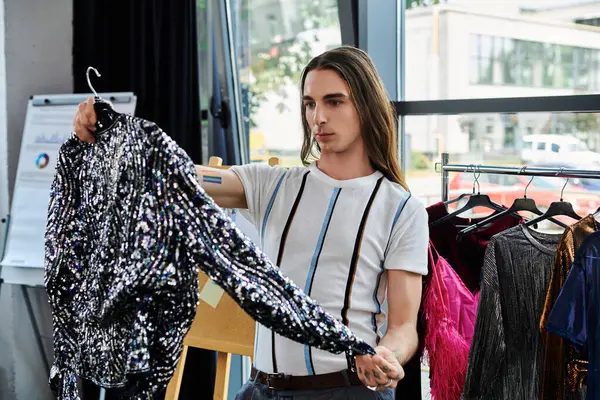 A young man examines a garment in his atelier, working on giving new life to old clothing. — Stock Photo