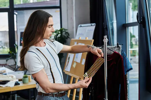 A young man, showcasing a piece of clothing restoration, in a light-filled atelier setting, focused on upcycling and sustainability. — Stock Photo