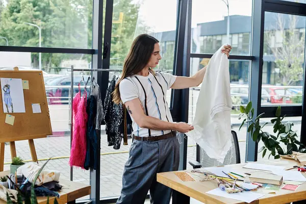 A young gay man in his atelier, examining a garment hes restoring, showcasing his dedication to sustainable fashion and giving discarded clothing new life. — Stock Photo