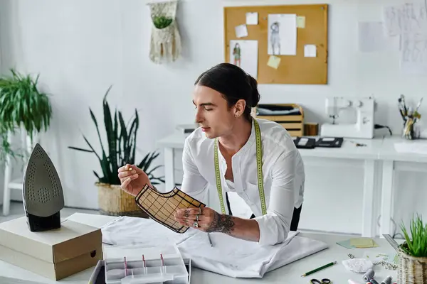 A young man in a white shirt examines a fabric pattern, showcasing his dedication to sustainable fashion restoration in his atelier. — Stock Photo