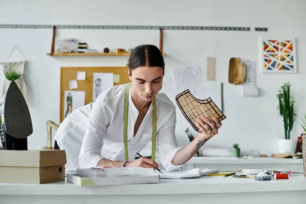 Un joven con una camisa blanca examina cuidadosamente un pedazo de tela en su taller de restauración de ropa de bricolaje, comprometido a dar nueva vida a la ropa desechada. — Stock Photo