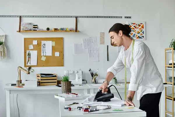 A young tailor in a white shirt carefully irons a garment in his DIY clothing restoration atelier, focused on giving new life to old items. — Stock Photo