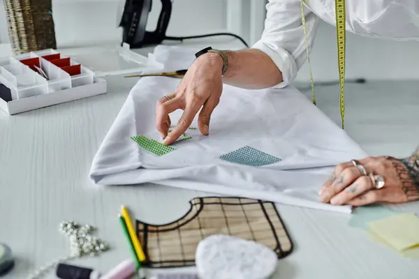 A young man, owner of a DIY clothing restoration atelier, meticulously applies embellishments to a white shirt. — Stock Photo