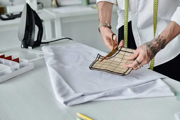 A young man, wearing a white shirt and a measuring tape, cuts fabric in his atelier. He is focused on sustainability and reviving old clothing. — Stock Photo