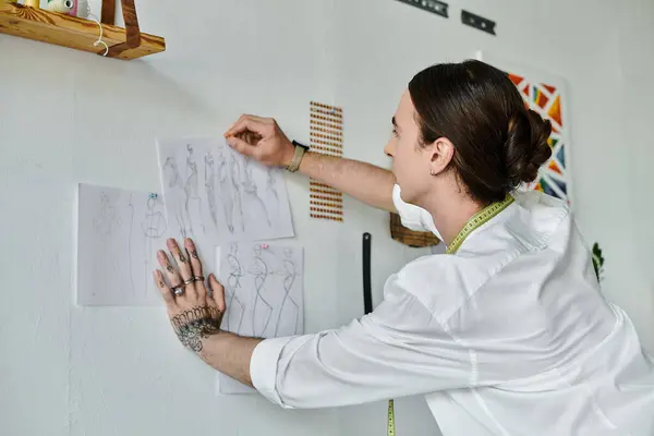 A young man with a tattoo arranges sketches for a clothing restoration atelier. — Stock Photo