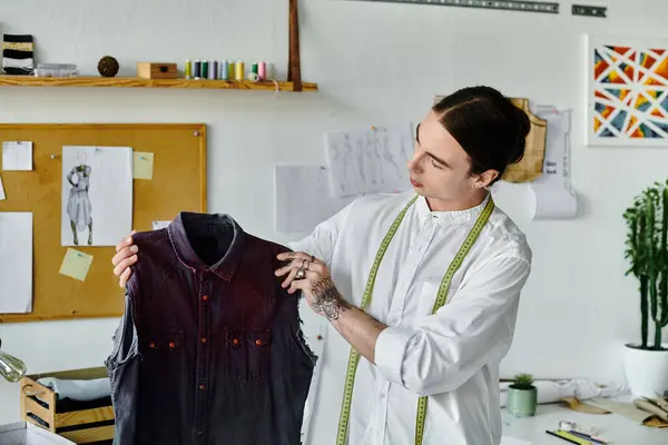 A young man examines a discarded piece of clothing, ready to give it a new life in his sustainable fashion atelier. — Stock Photo