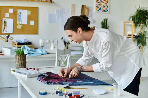 A young man in a white shirt meticulously sews a piece of clothing in his DIY clothing restoration atelier. — Stock Photo