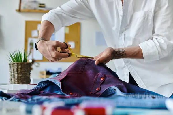Um jovem de camisa branca corta jeans descartados em seu atelier de restauração sustentável de roupas. — Fotografia de Stock
