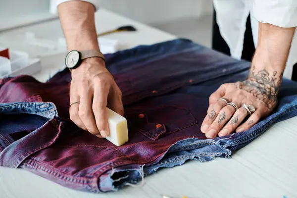 A young man restores a worn denim shirt in his DIY clothing atelier, embodying sustainable fashion through creative revitalization. — Stock Photo