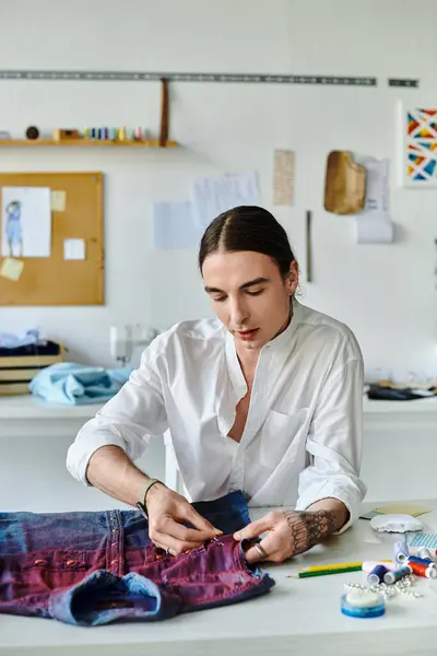 A young man meticulously repairs a vintage denim shirt in his sustainable clothing restoration atelier. — Stock Photo