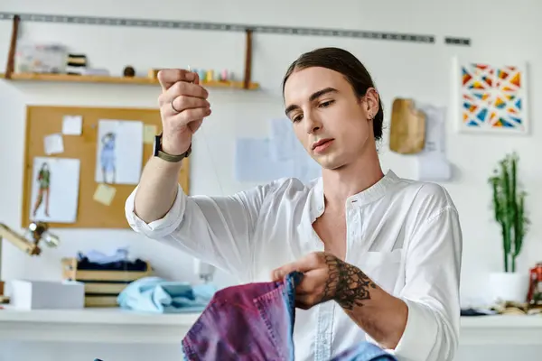 A young man in a white shirt meticulously threads a needle, focusing on his craft of reviving discarded clothing in his DIY clothing atelier. — Stock Photo