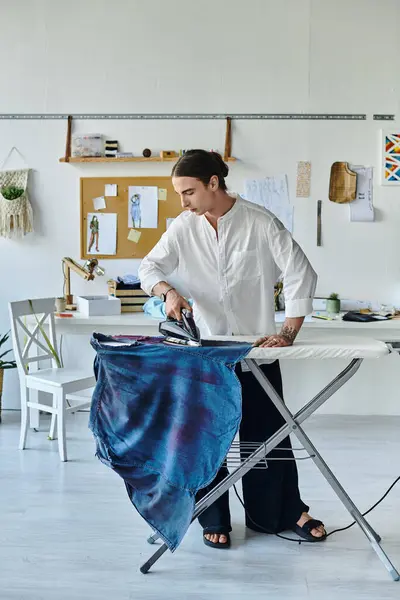 A young man in a white shirt is ironing a blue garment in his DIY clothing restoration atelier. — Stock Photo