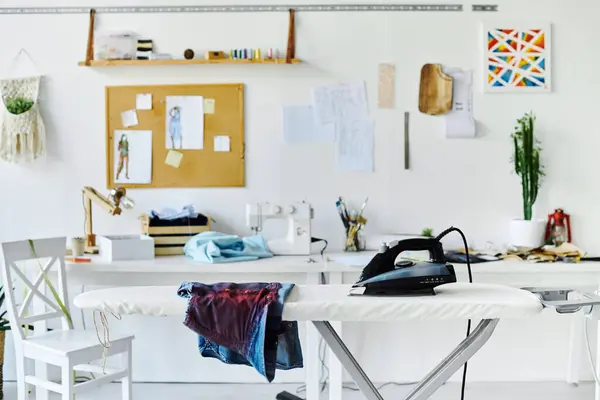 A clean and well-lit workspace, featuring an ironing board with a garment laid out, an iron, and a sewing machine in the background. — Stock Photo