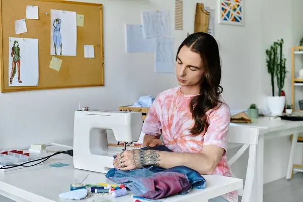 Un joven se sienta en su máquina de coser, centrado en reparar y restaurar la ropa en su taller de bricolaje sostenible. - foto de stock