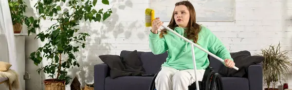 A young brunette woman in a wheelchair sits in her living room, holding a broom in her hands. — Stock Photo