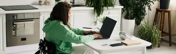 A young woman in a wheelchair is working on her laptop in her living room. — Stock Photo