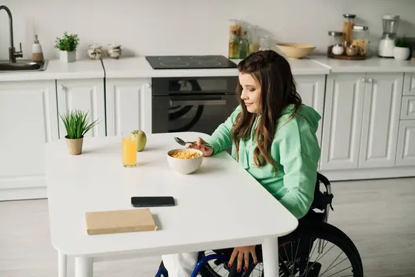 A young woman in a wheelchair sits at a kitchen table, enjoying a bowl of cereal and a glass of juice. — Stock Photo