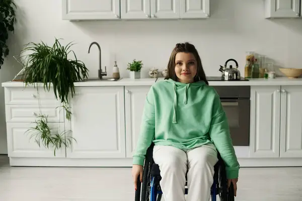 Eine brünette junge Frau im Rollstuhl sitzt in ihrer Küche und lächelt in die Kamera. — Stockfoto