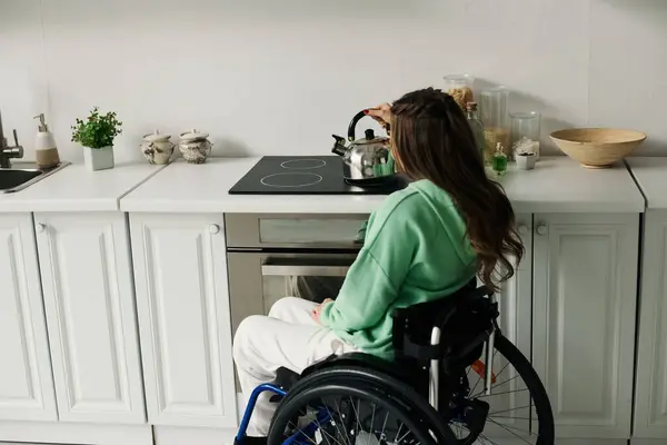 Une jeune femme en fauteuil roulant prépare le thé à la maison dans sa cuisine. — Photo de stock