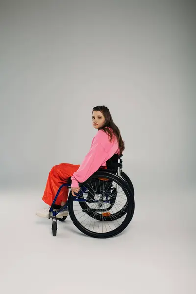 Girl in wheelchair looking at camera on grey background, inclusion and disability — Stock Photo