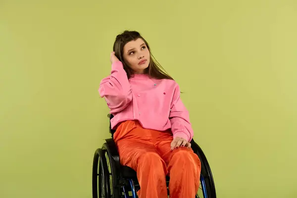 Une jeune femme brune contemplative avec un handicap, assise dans un fauteuil roulant, pose la tête dans sa main dans un cadre de studio. — Photo de stock