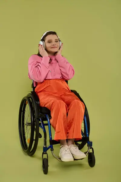 Молода брюнетка з інвалідністю сидить в інвалідному візку в студії, носить повсякденний одяг і слухає музику. — стокове фото