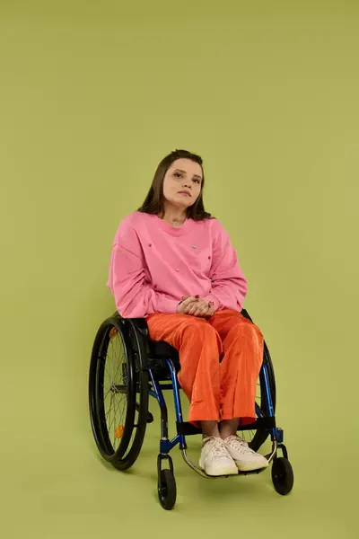 A young brunette woman with a disability sits in a wheelchair in a studio setting. She is wearing casual clothing and looking at the camera. — Stock Photo