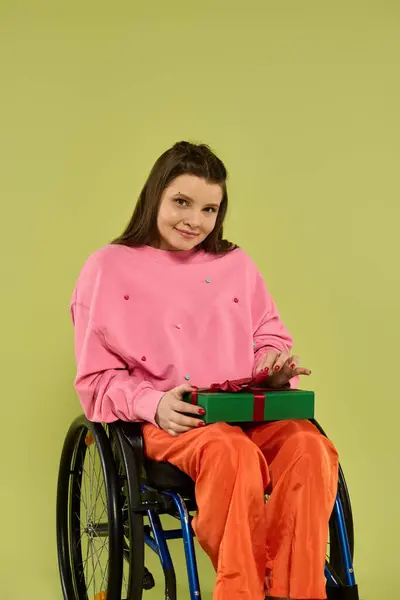 A young brunette woman in a wheelchair opens a green gift box in a studio setting. — Stock Photo