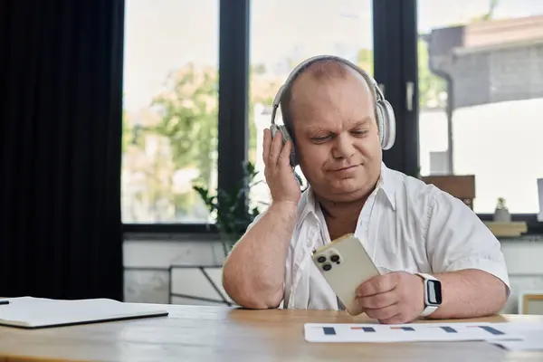 A man with inclusivity in an office setting, wearing headphones and holding a smartphone. — Stock Photo