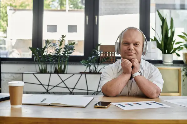 A man with inclusivity wearing headphones sits at a desk with his hands clasped, looking calmly at the camera. — Stock Photo