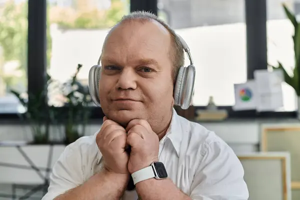 A man with inclusivity wearing headphones sits in a contemporary office setting, lost in thought. — Stock Photo