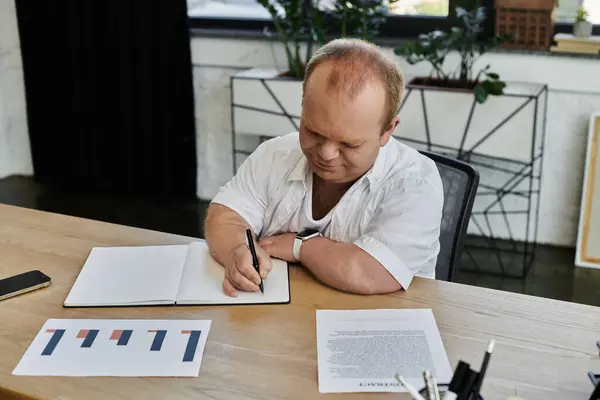 Un uomo con inclusività siede a una scrivania in un ufficio, concentrandosi sul suo lavoro. — Foto stock