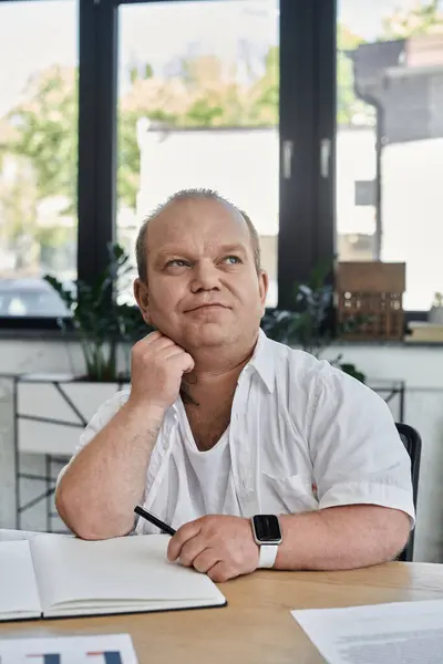 Мужчина с включённостью в белой рубашке сидит за столом в офисе, размышляя о дневной работе.. — стоковое фото