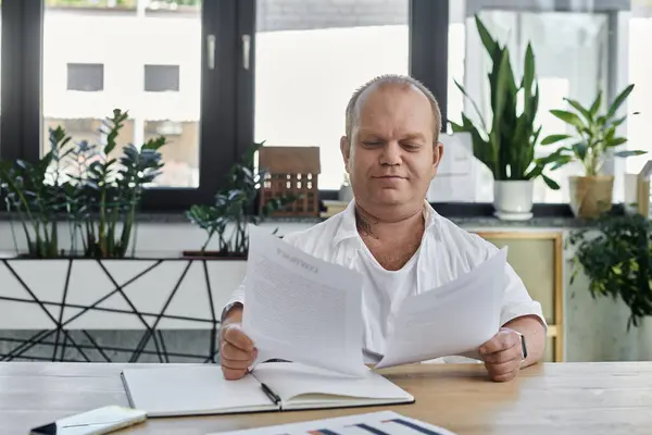 A man with inclusivity sits at a desk in an office reviewing paperwork. — Stock Photo