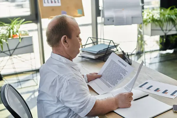 A man with inclusivity sits at a desk in an office, reviewing a contract. — Stock Photo
